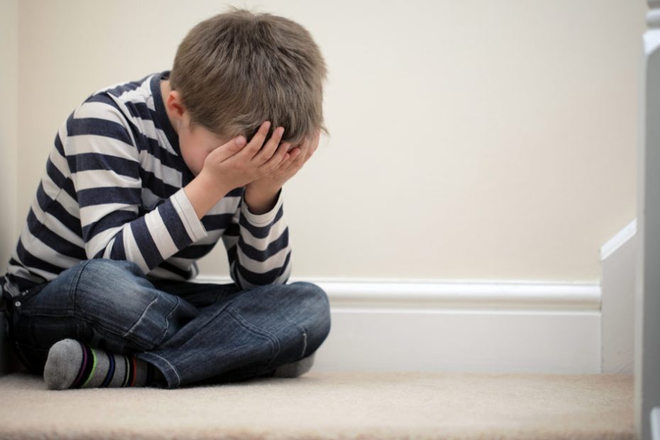 young child sat on stairs all alone crying with head in hands